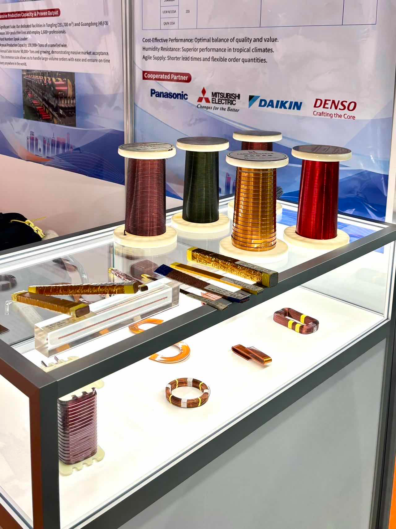 Corporate capacity infographic: large facility areas, 100,000+ tons enameled wire capacity, 90,000+ tons annual sales, value & reliability claims, partner logos Panasonic, Mitsubishi Electric, Daikin, Denso.